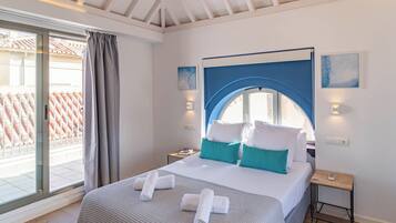 Habitación de hotel con cama, mesita de noche, ventana con cortinas y vista a un tejado de tejas rojas.