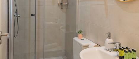 Une salle de bain moderne avec une douche en verre, des toilettes blanches, un lavabo avec des articles de toilette et une petite plante en pot.