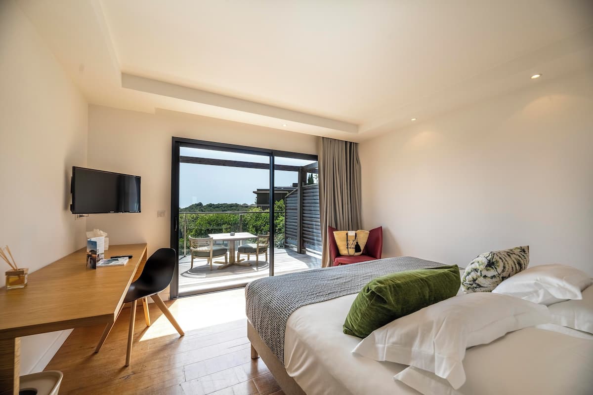 Une chambre d’hôtel moderne dotée d’un grand lit, d’un bureau, d’une télévision et d’un balcon avec une table et des chaises.