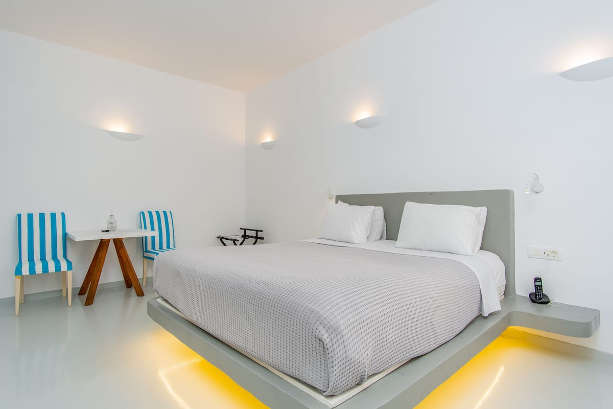 A modern bedroom with a large bed, bedside tables, a small desk, and chairs.