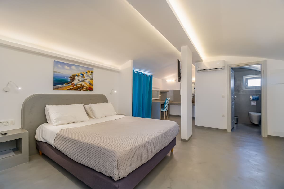 A modern bedroom with a large bed, a desk, and a bathroom visible through an open door.