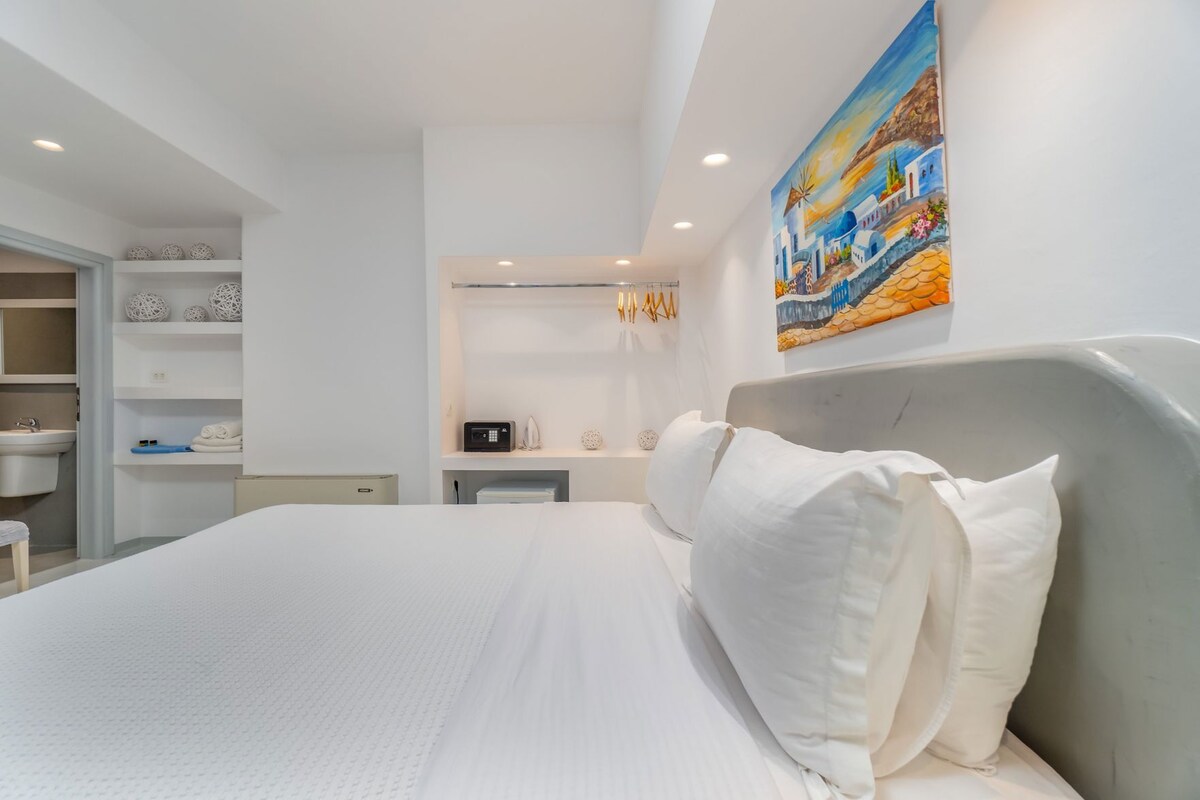 Una habitación de hotel moderna con una cama grande, un escritorio integrado, un baño con lavamanos y un cuadro en la pared.