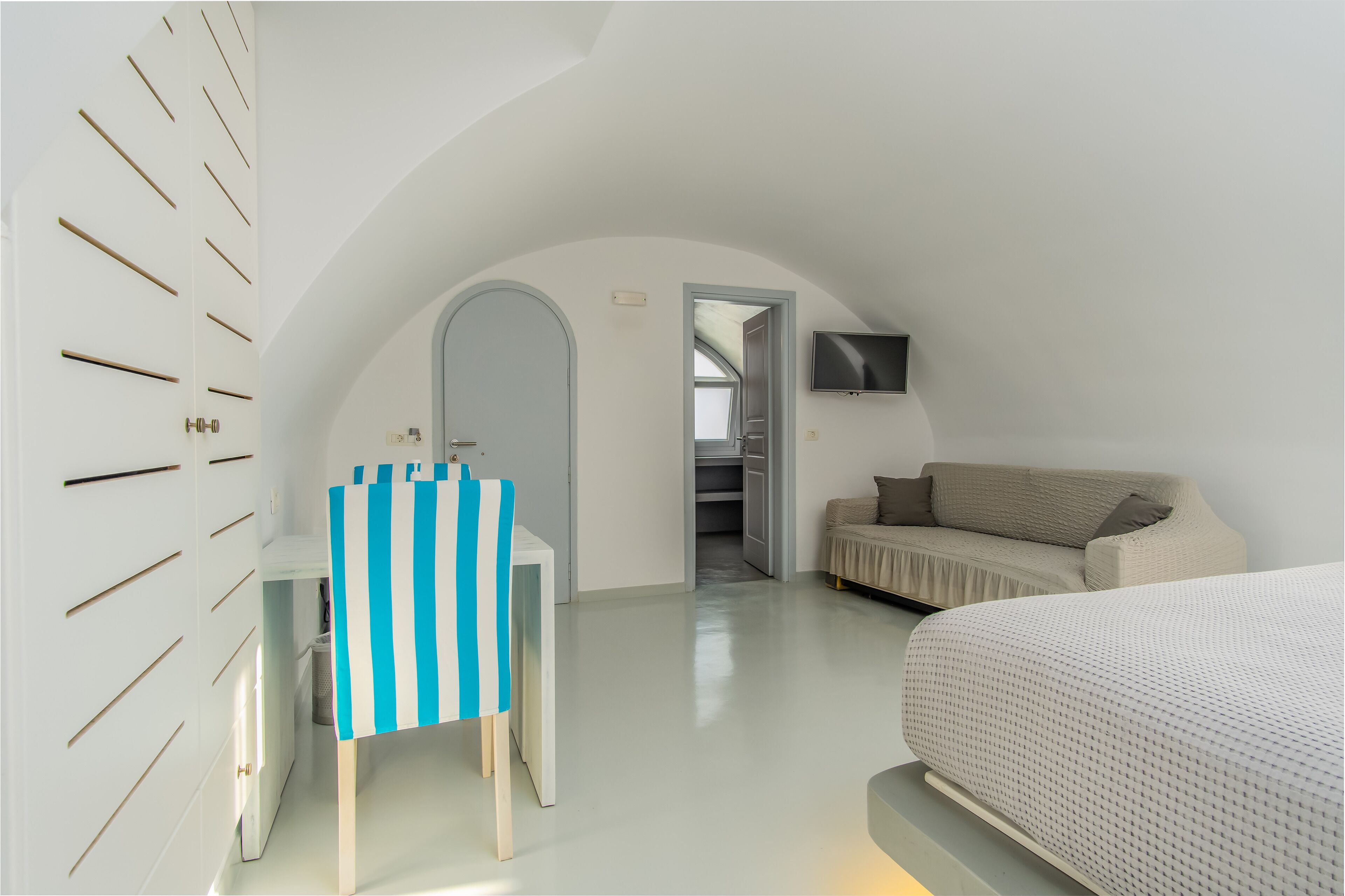 A bedroom with a bed, a sofa, a TV, and a desk with a striped chair.