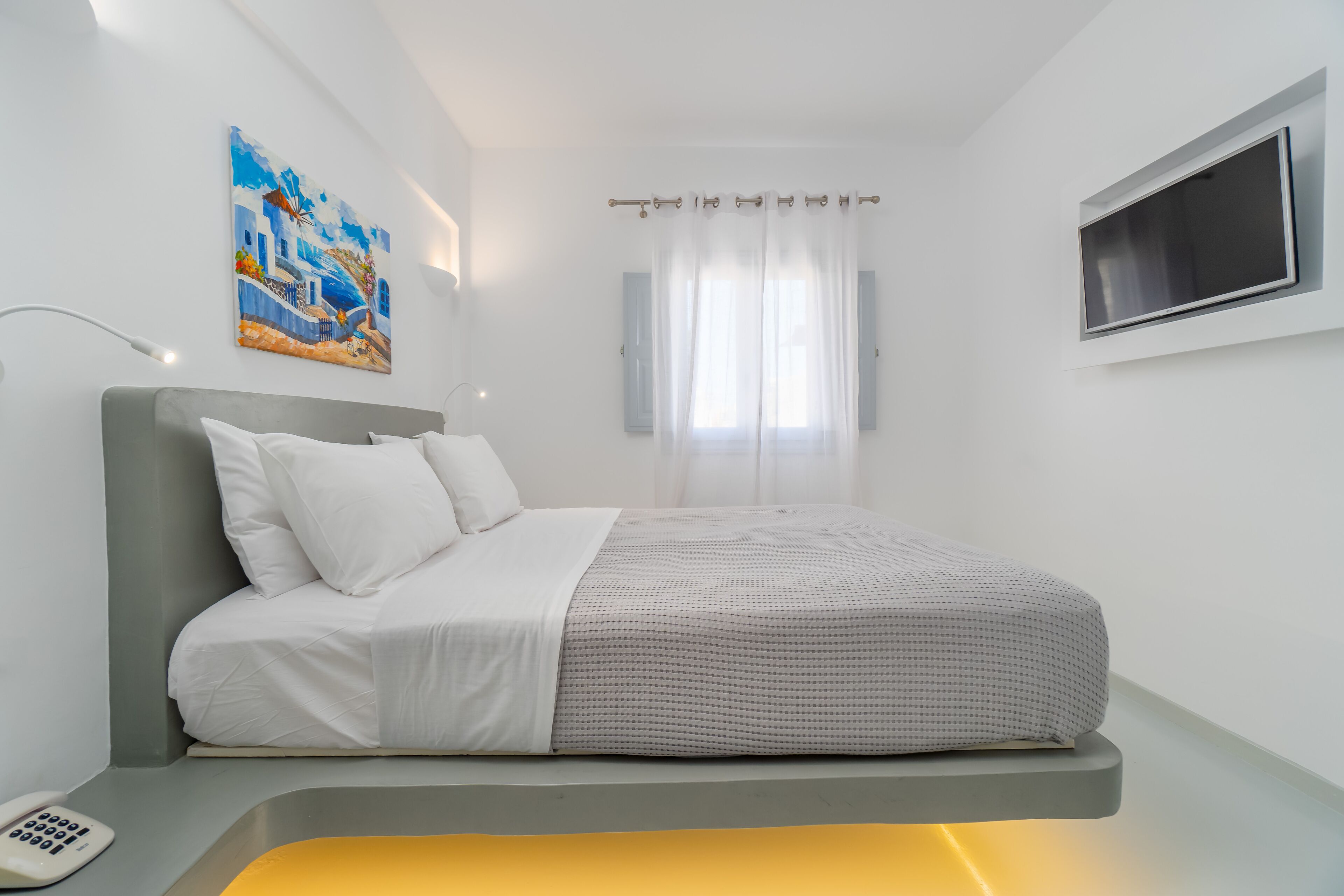 Un dormitorio moderno con una cama, una mesita de noche, un control remoto y un cuadro en la pared.