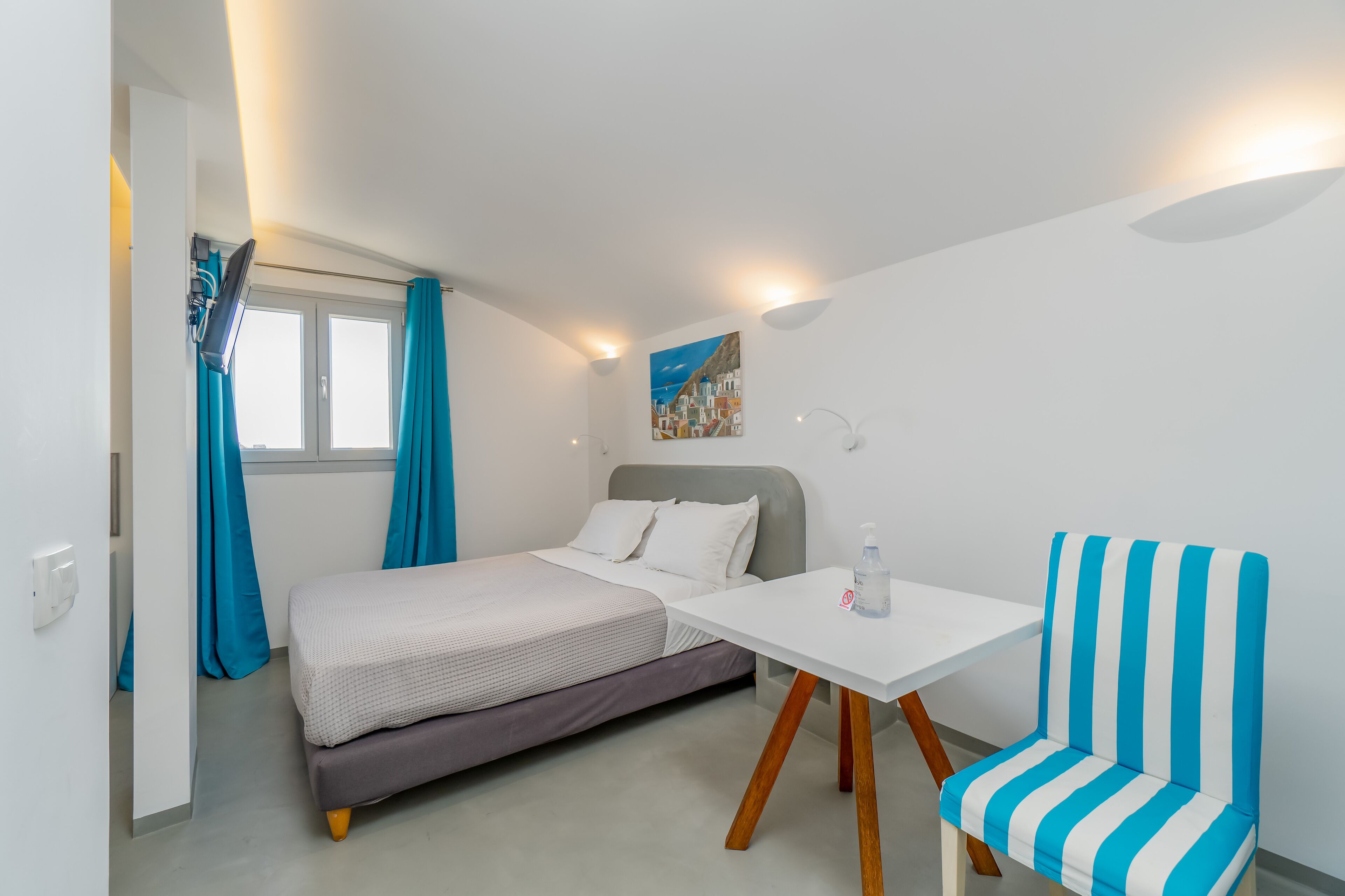 Quarto compacto com cama, uma mesinha e uma cadeira listrada.