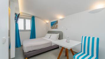 Quarto compacto com cama, uma mesinha e uma cadeira listrada.