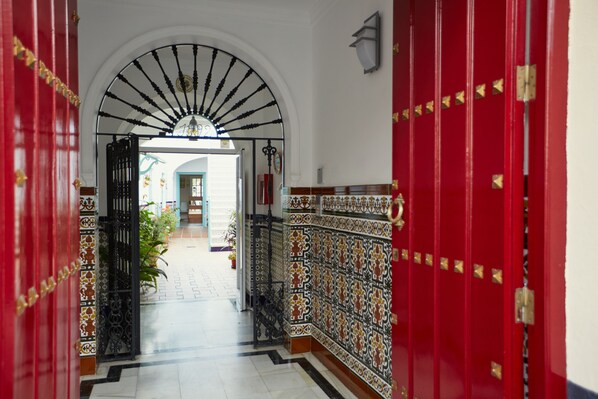 A hallway with a red door, a white wall, and a tiled floor.
