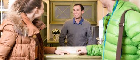 A reception desk with a man holding a map, a woman in a brown jacket, and another person in a green jacket.