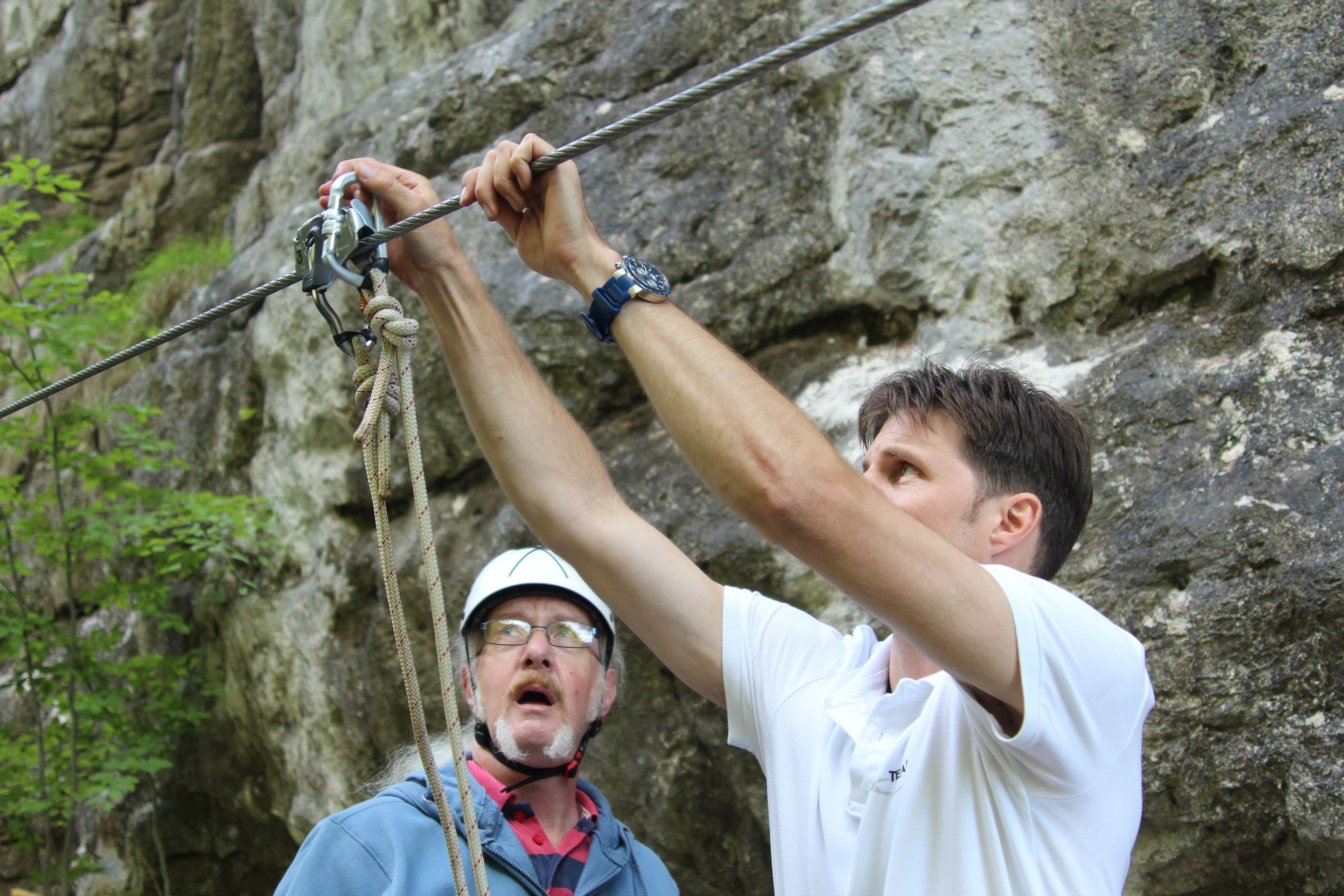 A person climbing a rope with a rocky background.