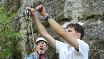 A person climbing a rope with a rocky background.