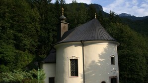 Une petite église blanche, dotée d’un clocher et d’une coupole, entourée d’une végétation luxuriante et de montagnes.