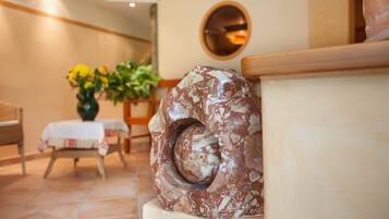 Une sculpture en marbre dans un hall d’entrée, avec un grand miroir rond au mur, une table ornée d’un vase de fleurs et un banc en bois.