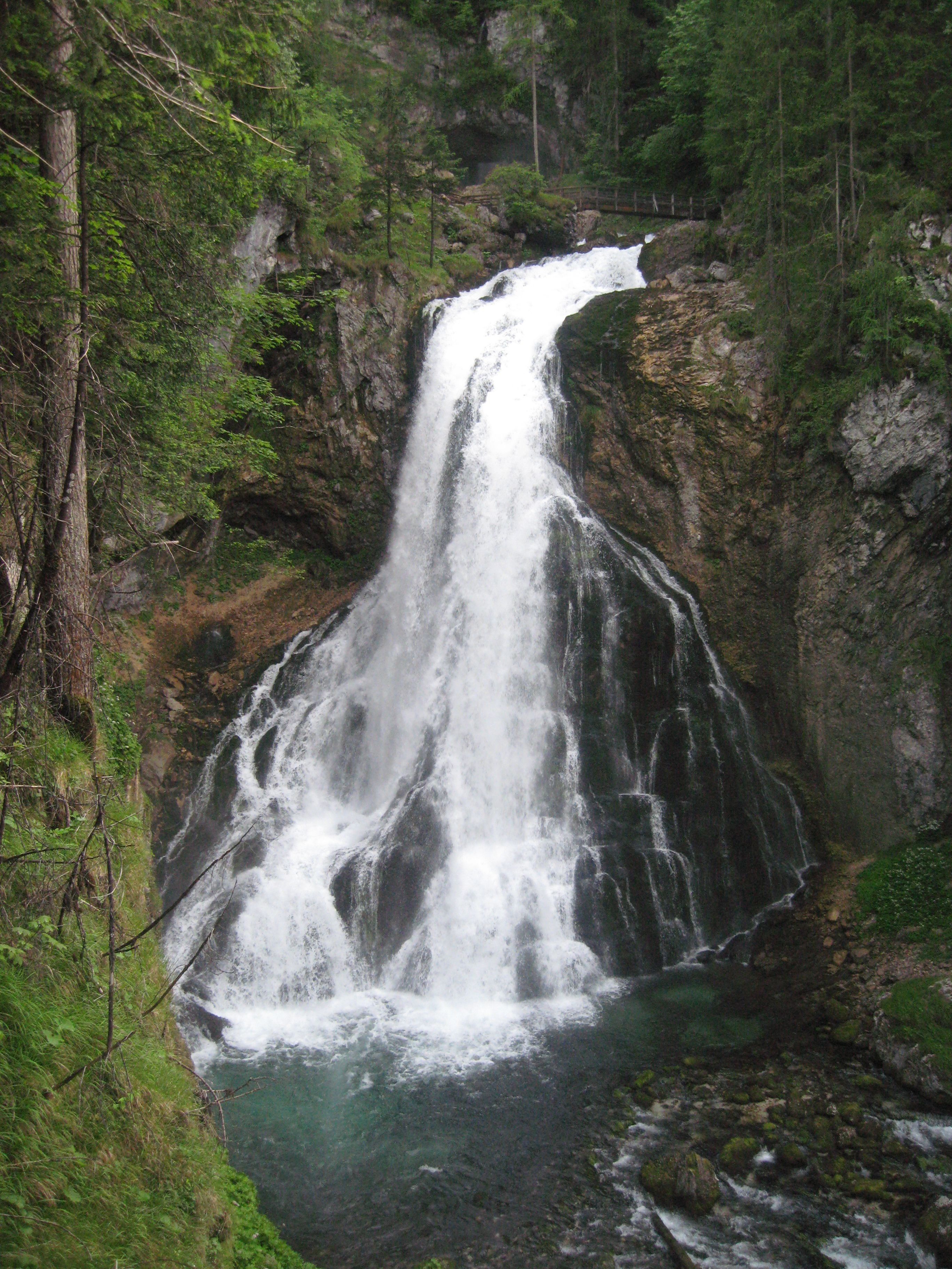 Ein Wasserfall stürzt über eine steile Felswand, umgeben von dichtem Wald.