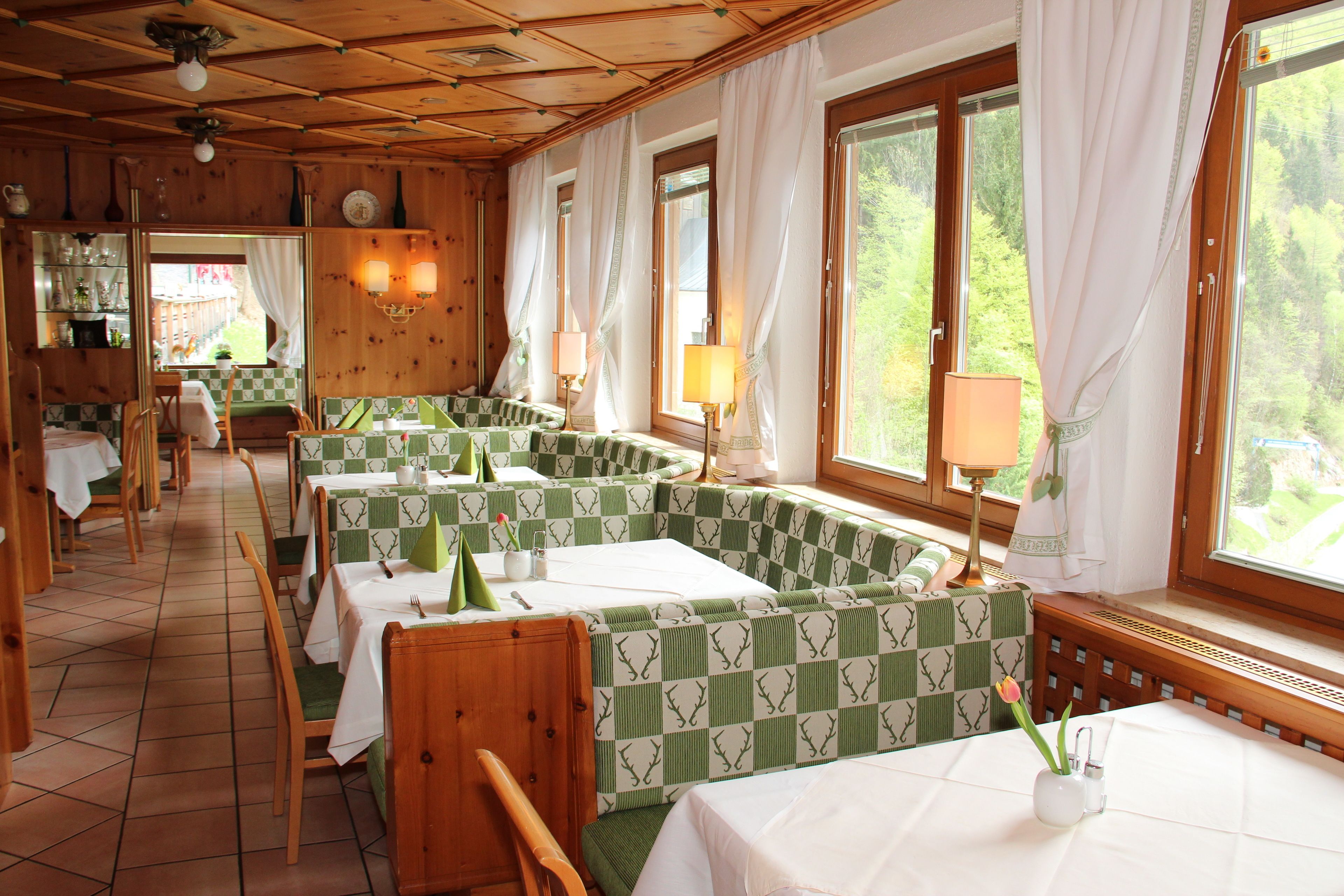 Un restaurant aux murs en bois, avec des banquettes à carreaux verts et blancs et de grandes fenêtres ornées de rideaux.