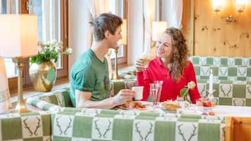 Ein Paar speist an einem Tisch mit kariertem Tuch, umgeben von grün gemusterten Kissen.