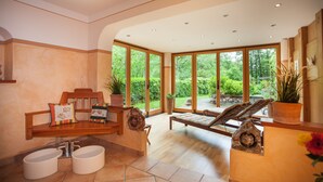 Une salle de spa avec un banc en bois, une petite table sur laquelle se trouve un bol, et une grande fenêtre donnant sur un paysage verdoyant.