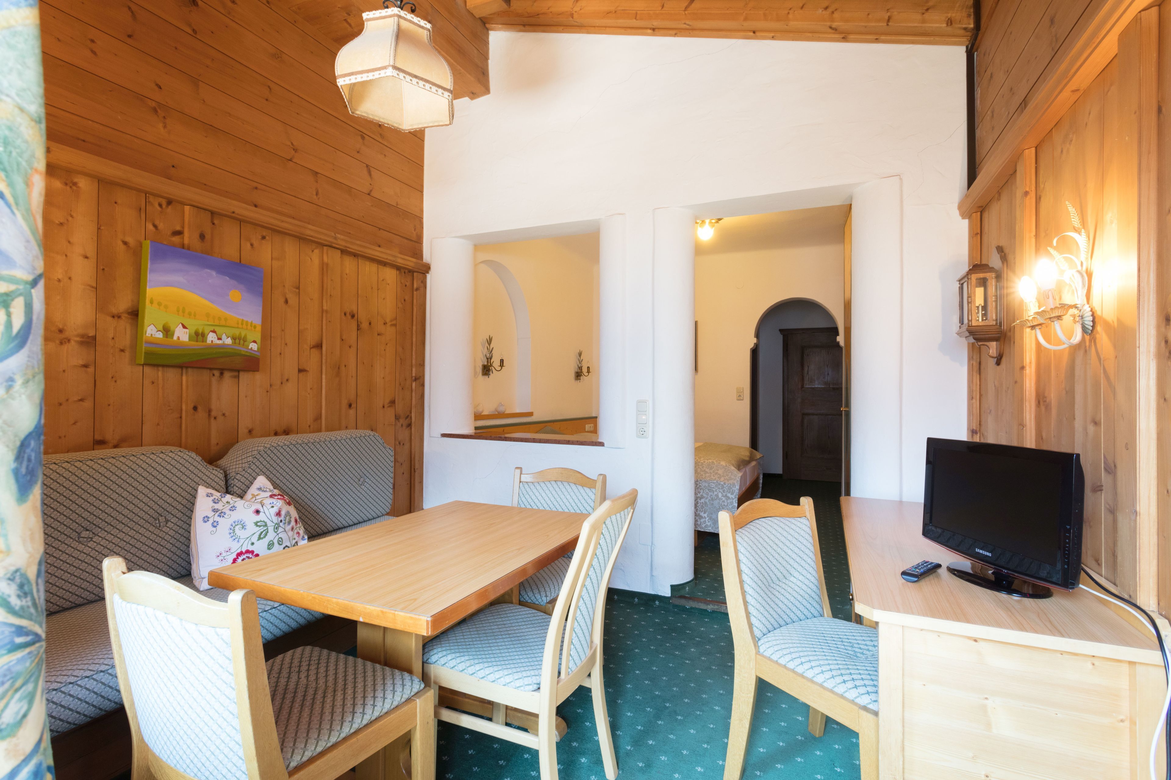 A cozy room with a wooden ceiling, a dining table with chairs, a sofa, a television, and a painting on the wall.
