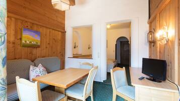 A cozy room with a wooden ceiling, a dining table with chairs, a sofa, a television, and a painting on the wall.