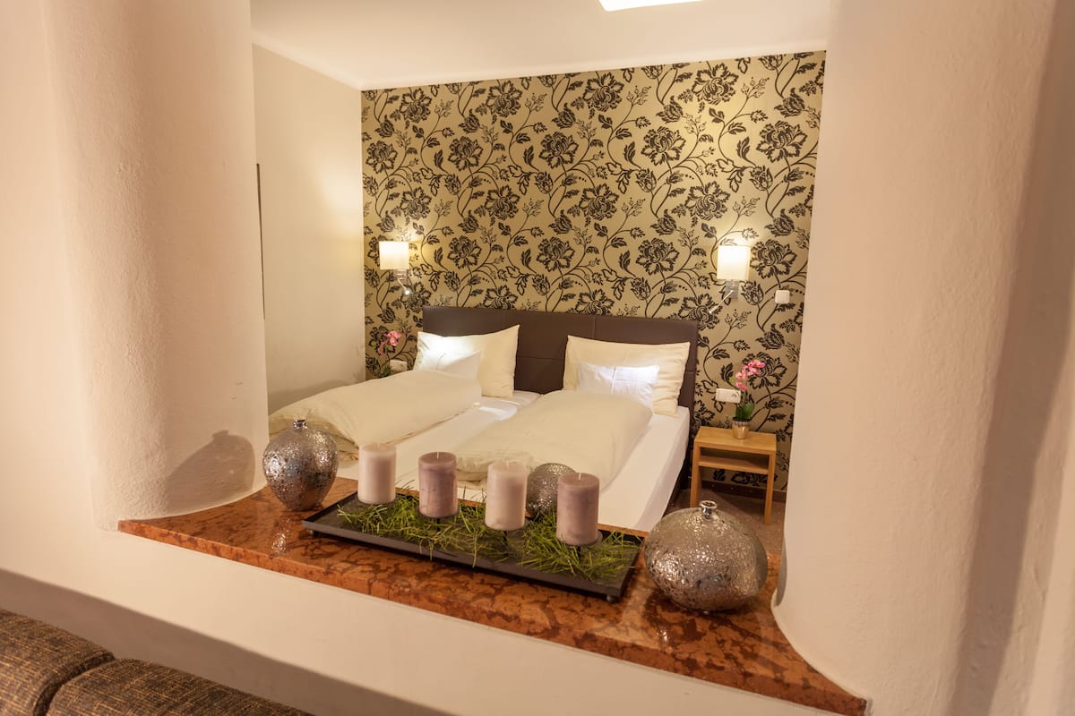 Een netjes ingerichte slaapkamer met een tweepersoonsbed, twee wandlampen en een decoratieve plank met kaarsen en een vaas.