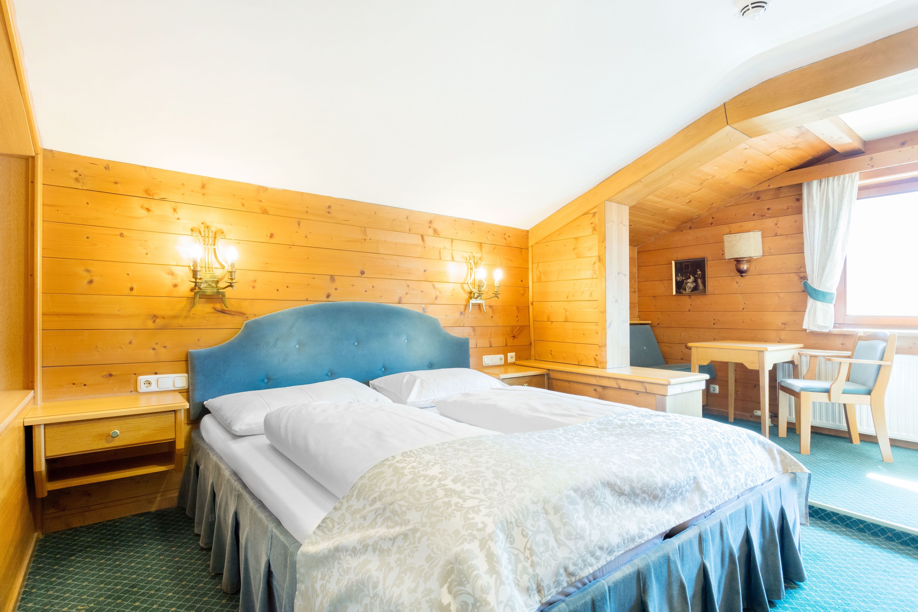 A wooden-paneled room with a bed, bedside tables, a desk, and a chair.