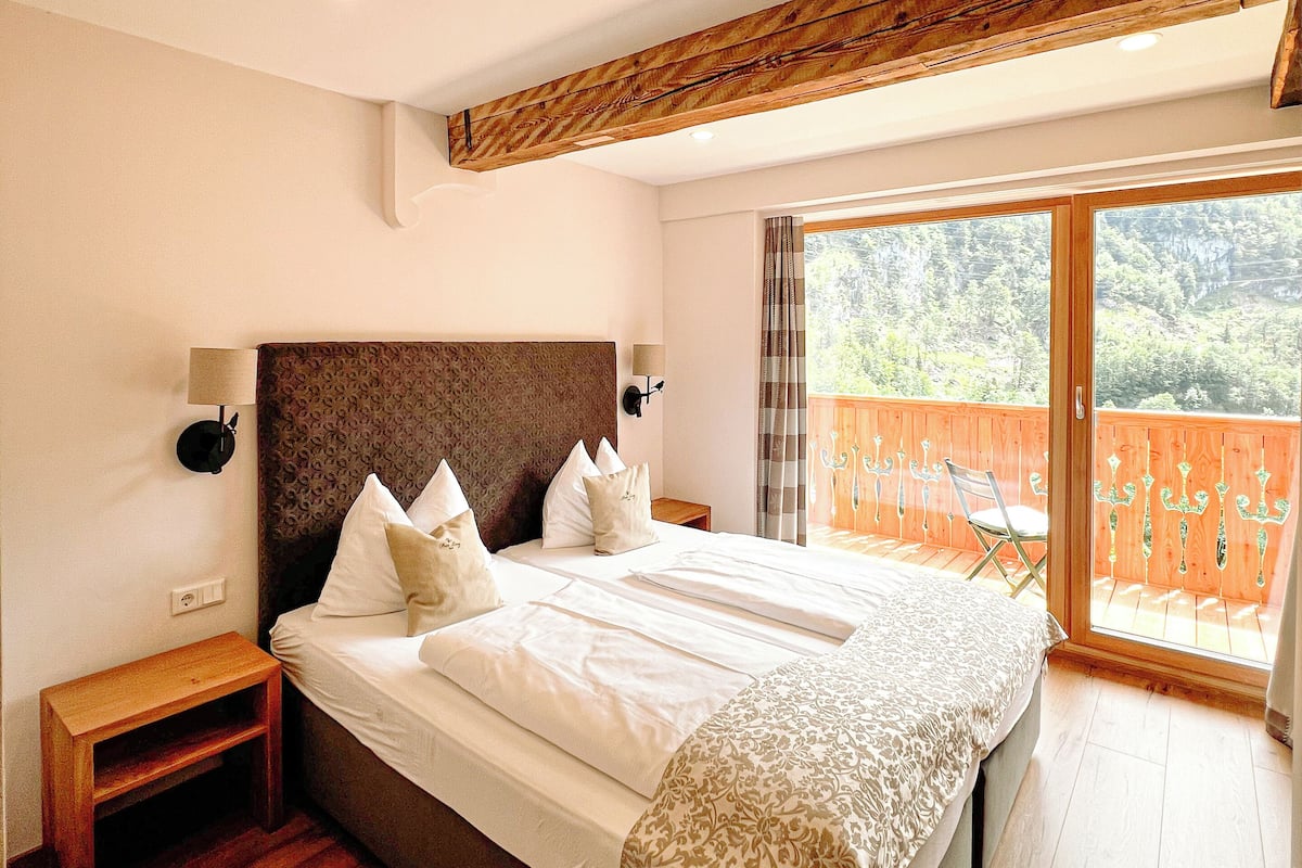 Een slaapkamer met een groot bed, een houten hoofdbord en uitzicht op een houten terras door een schuifdeur.