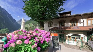 Un bâtiment avec une enseigne indiquant les types de chambres et les prix, un escalier menant à l’entrée et une vue sur les montagnes en arrière-plan.