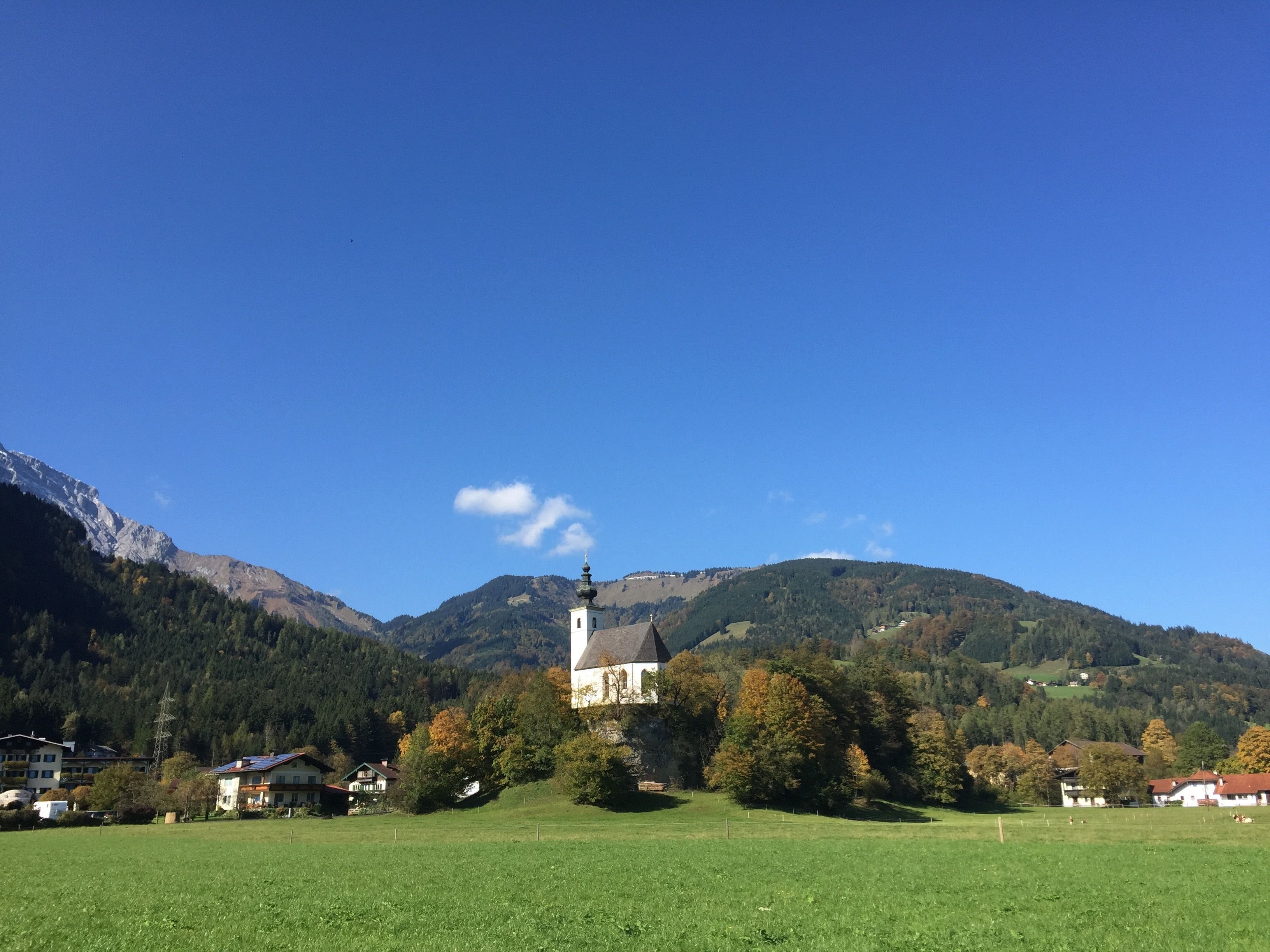 Una iglesia con un campanario rodeada por un campo verde y montañas al fondo.