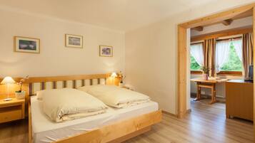 A bedroom with a wooden bed, bedside tables with lamps, a desk, and a chair. There are three framed pictures on the wall.