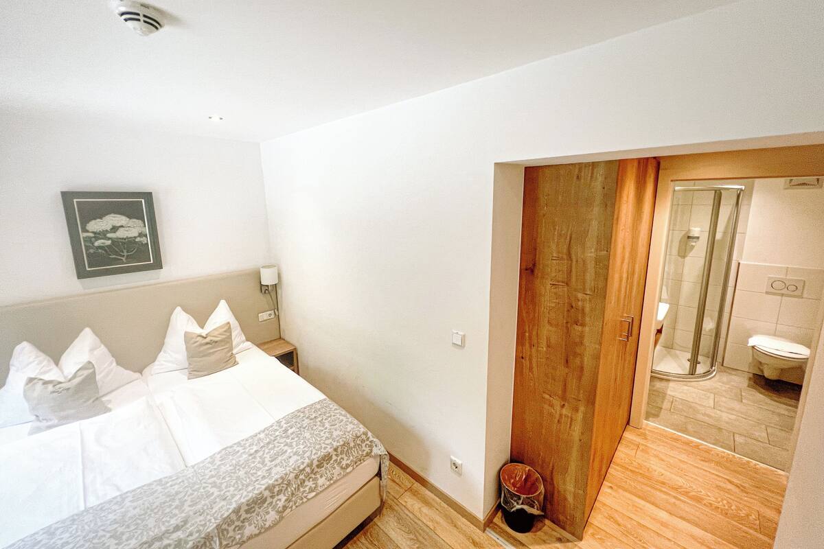 Een slaapkamer met een bed, een houten deur naar een badkamer en een lijst met een afbeelding aan de muur.