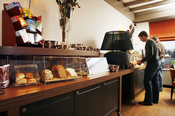 Mostrador de panadería con pan, pasteles, una máquina de café y una taza.