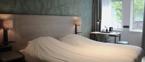 Habitación de hotel con una cama grande, dos lámparas de noche, un escritorio con una silla y una ventana con vistas a zonas verdes.