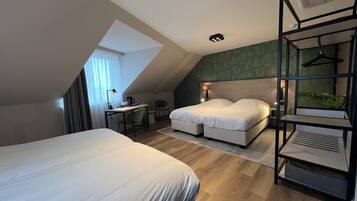 Una habitación de hotel moderna con techo inclinado, un escritorio con silla, dos camas, una mesita pequeña y un estante colgante.