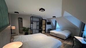 Een moderne slaapkamer met een groot bed, een klein bed, een bureau en een stoel. Er staat een plant, een spiegel en een kledingkast.