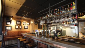Een bar met krukken, een toonbank en een wand vol drankflessen en glazen.