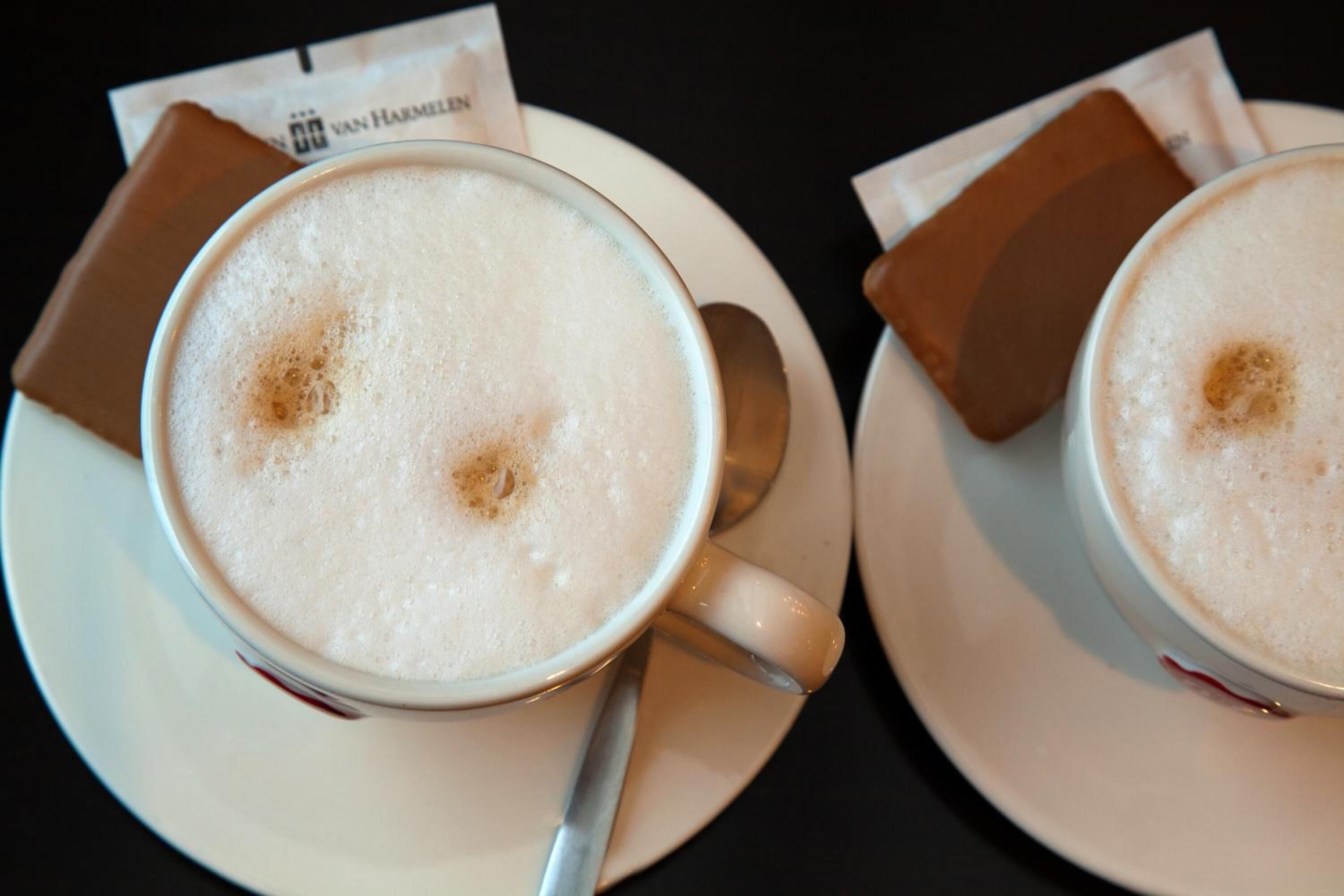 Two cups of coffee on white saucers with a spoon, placed on a table with a menu and a brown napkin.