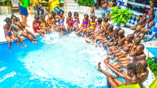 Um grupo de crianças sentadas ao redor de uma piscina, algumas espirrando água.
