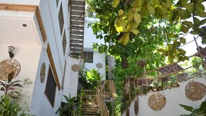 Uma escada estreita com guarda-corpos de madeira, cercada por vegetação exuberante e obras de arte decorativas na parede.