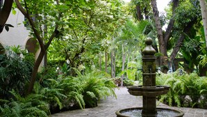 Un jardín con una fuente central, rodeado de exuberante vegetación y un sendero empedrado.