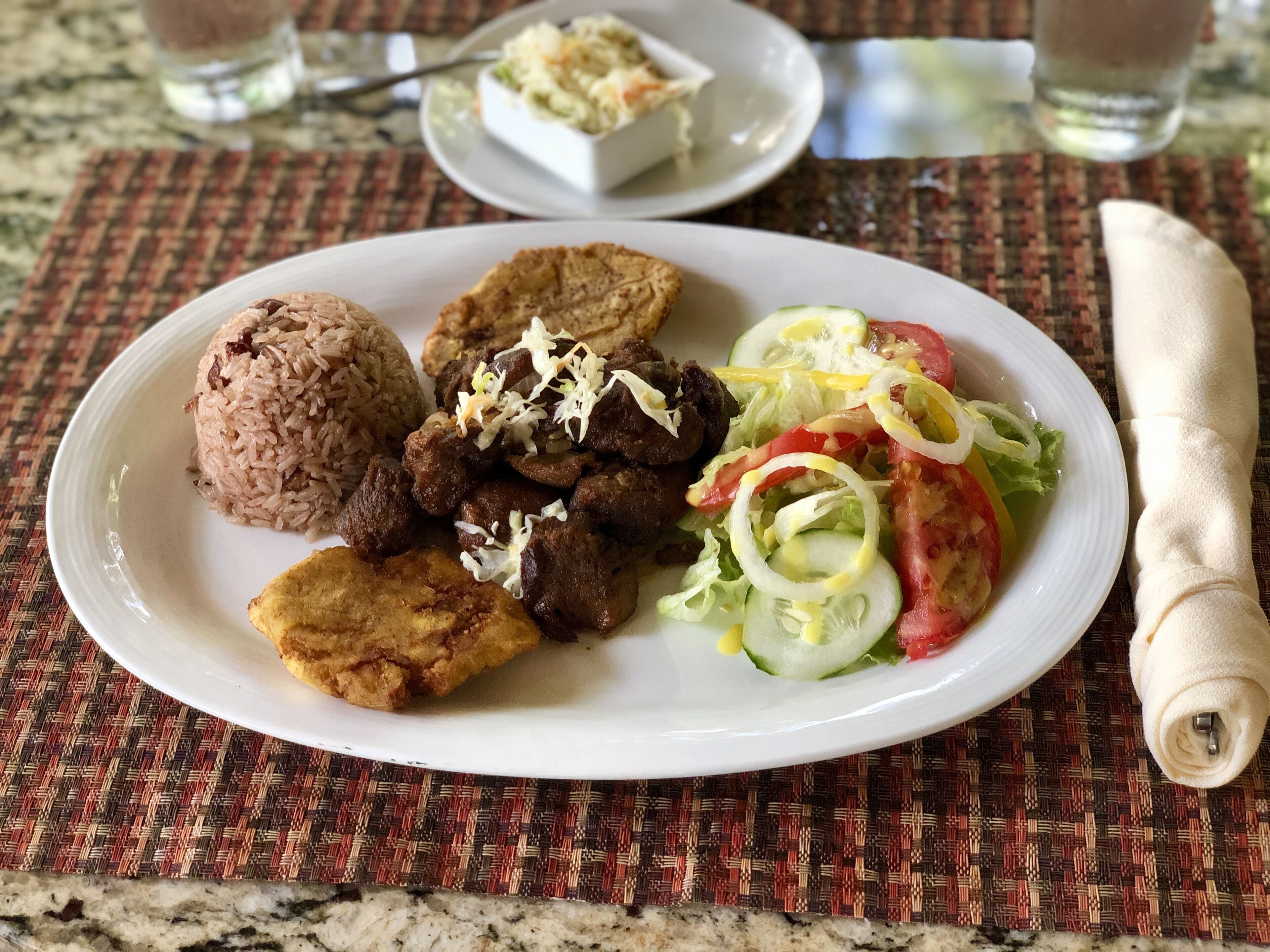 A plate with rice, meat, fried plantains, and a salad on a woven placemat.