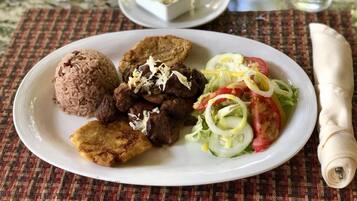 A plate with rice, meat, fried plantains, and a salad on a woven placemat.