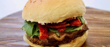 A burger with lettuce, red peppers, and a sesame seed bun on a wooden surface.