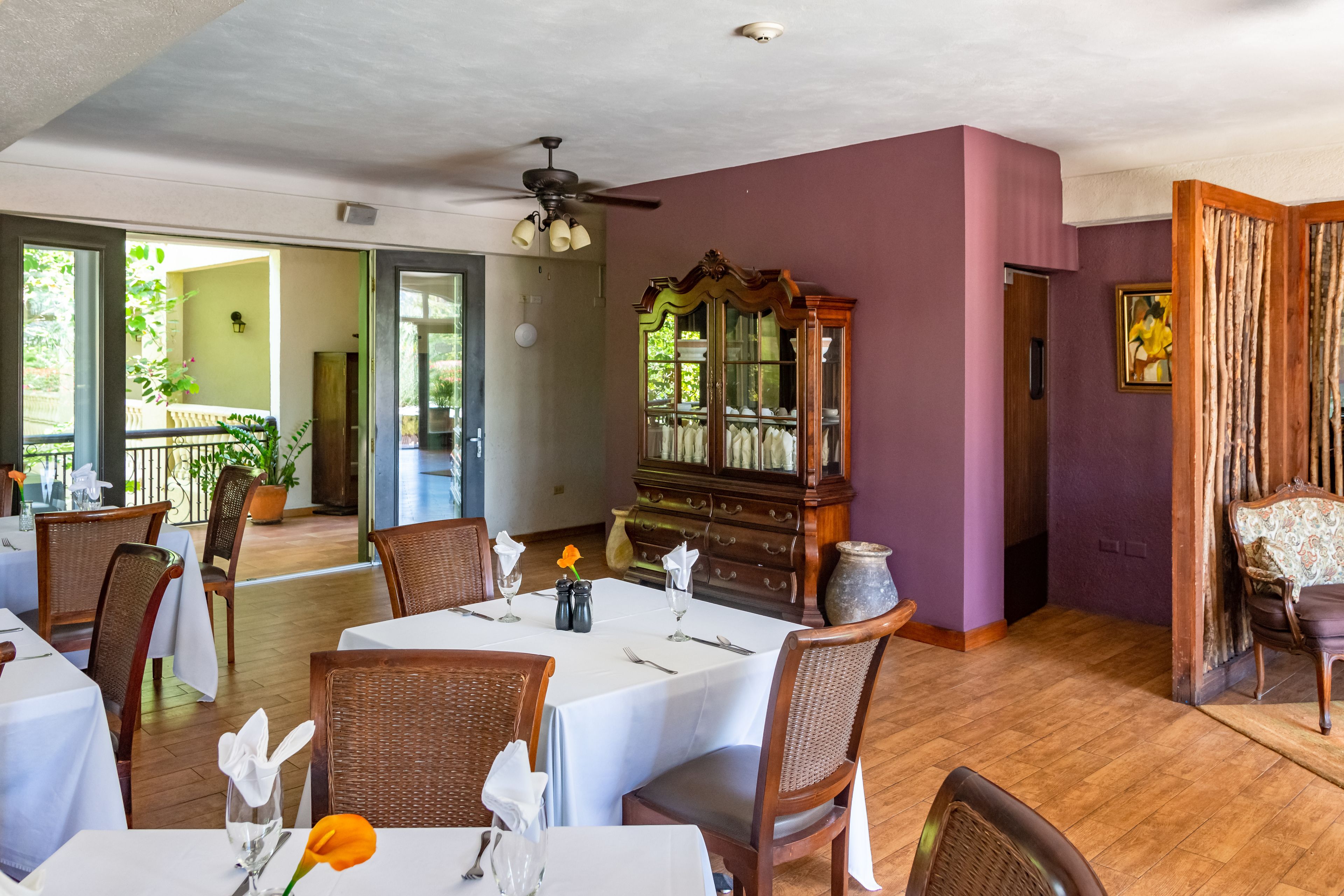 A dining area with tables set for service, a ceiling fan, and a large wooden cabinet.