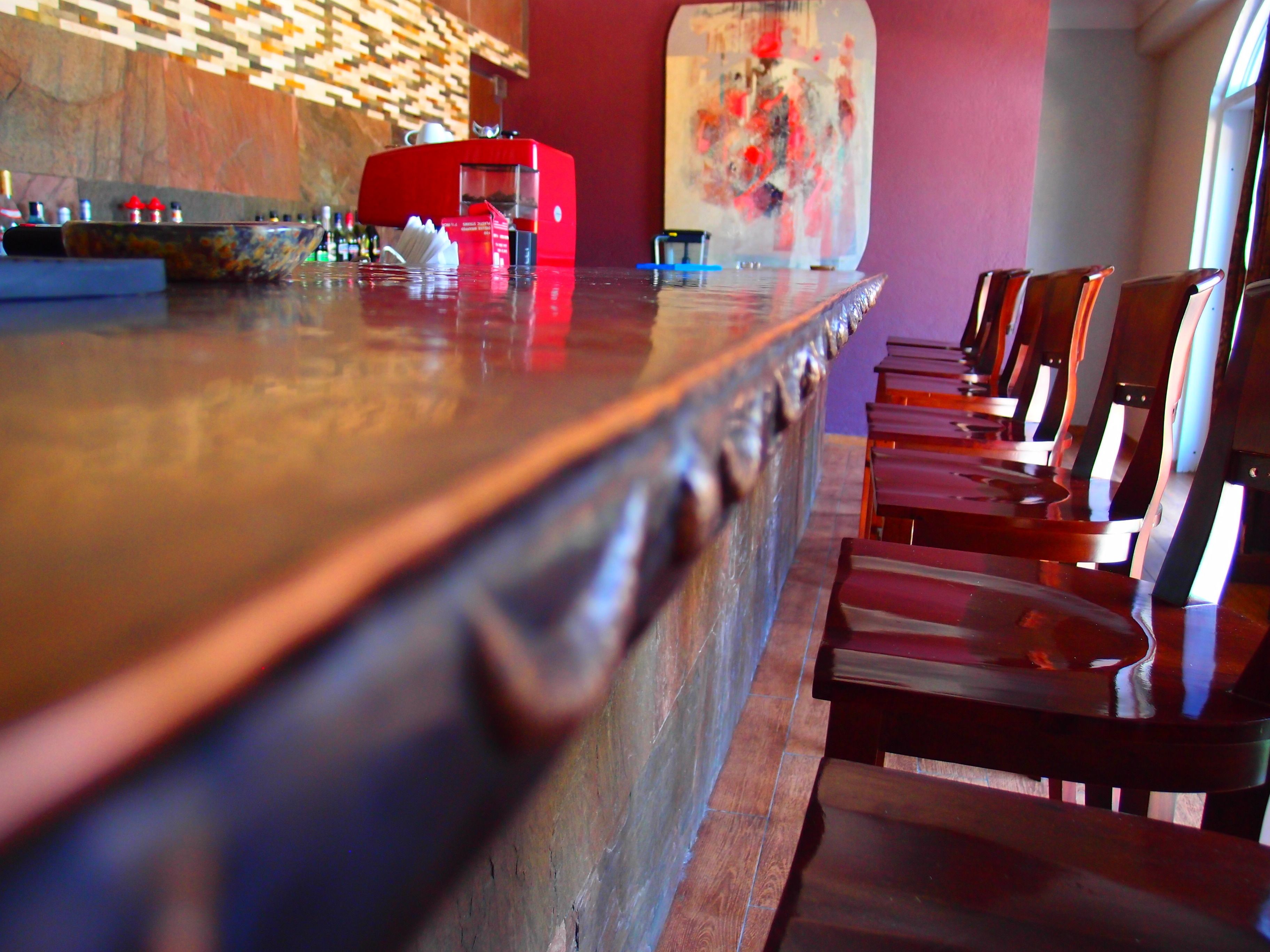 A bar area with a red coffee machine, wooden chairs, and a large abstract painting on the wall.