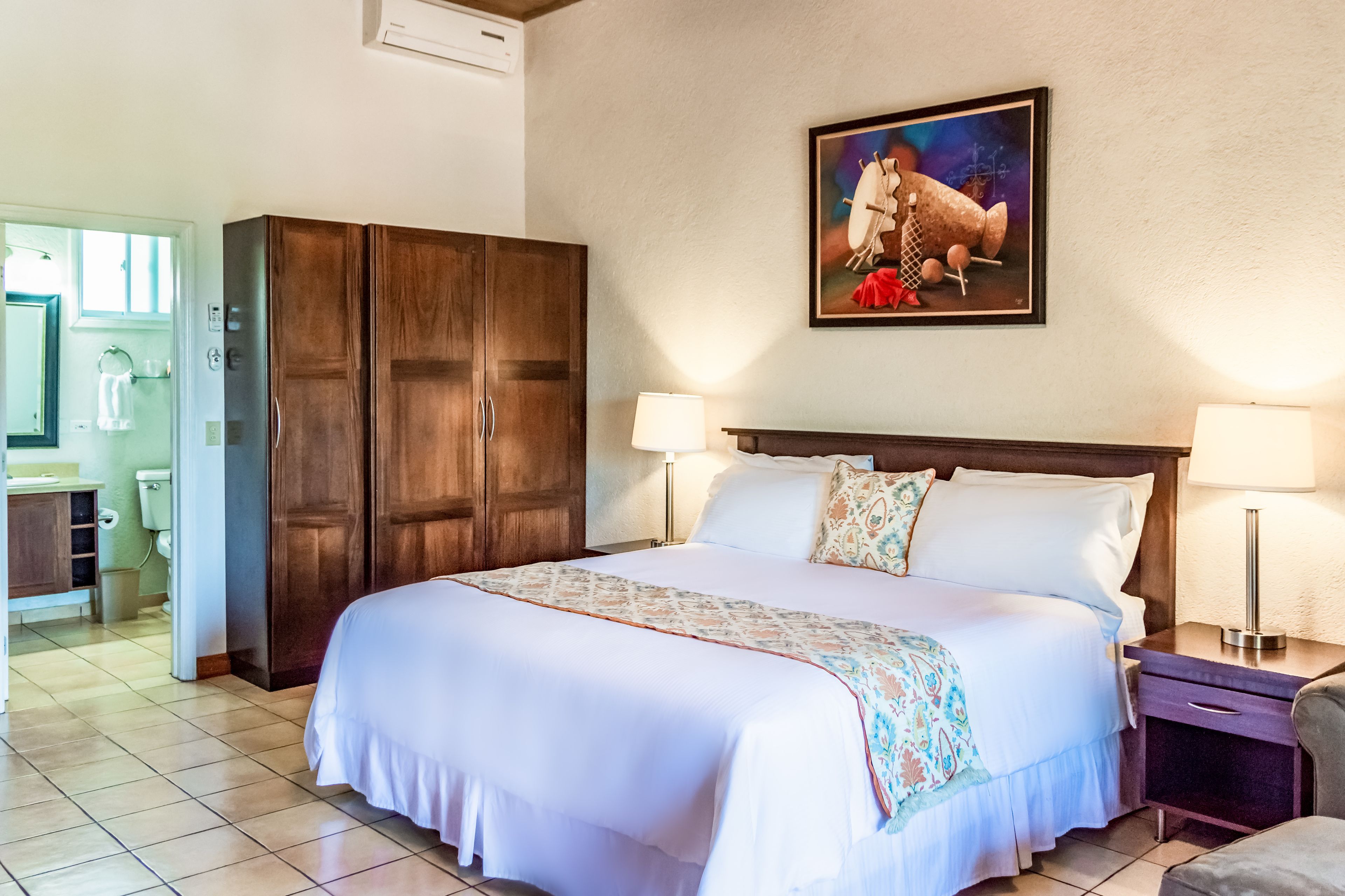 Una camera d'albergo con un letto grande, due lampade ai comodini, un armadio in legno e un quadro appeso al muro.