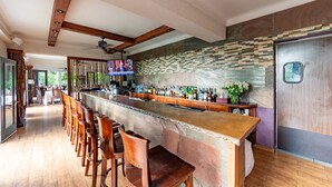 Una zona de bar con una barra alargada, varios taburetes y una pantalla de televisión.