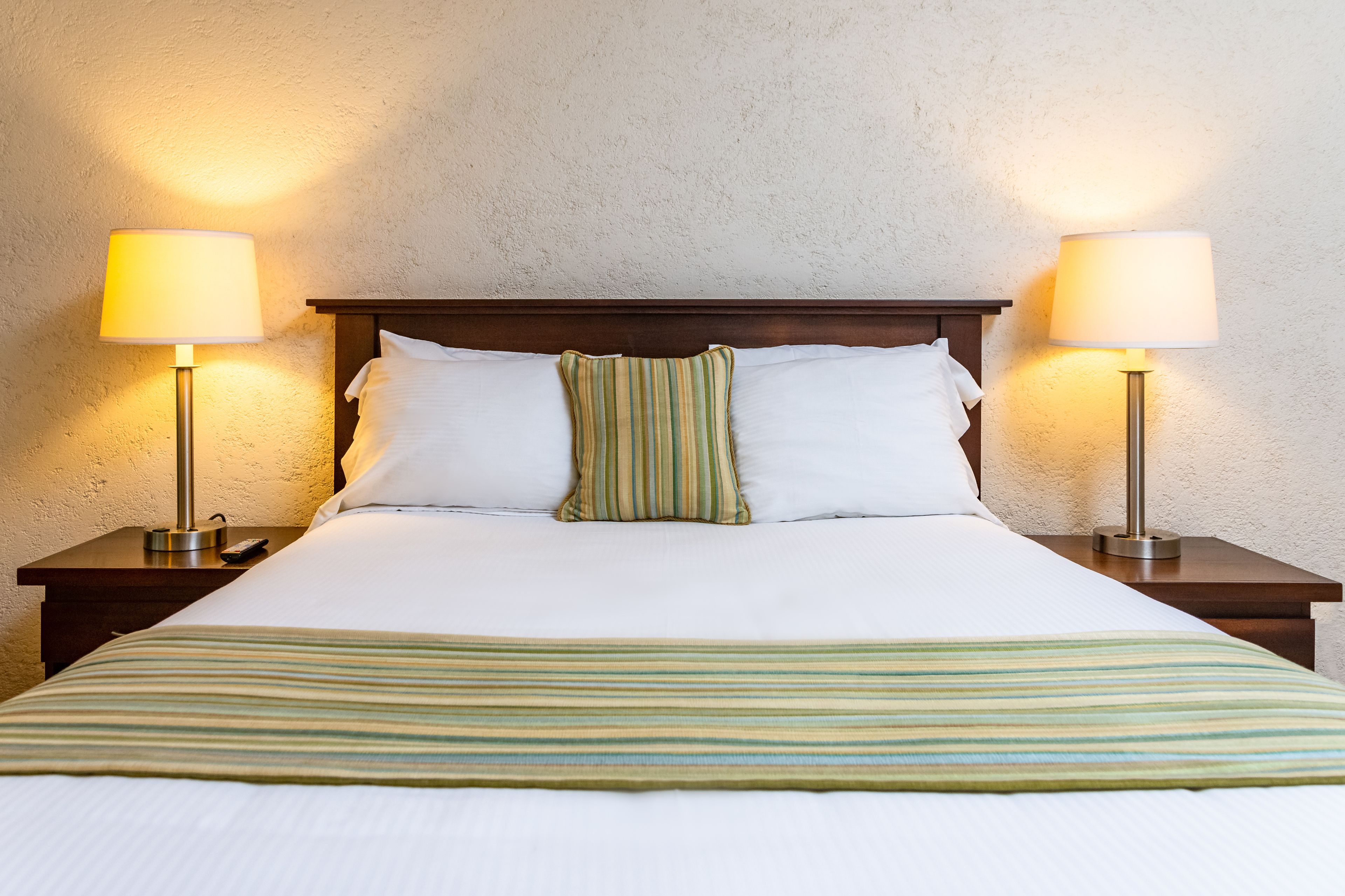 Una cama bien hecha con una colcha a rayas, dos lámparas de noche y un cabecero de madera.