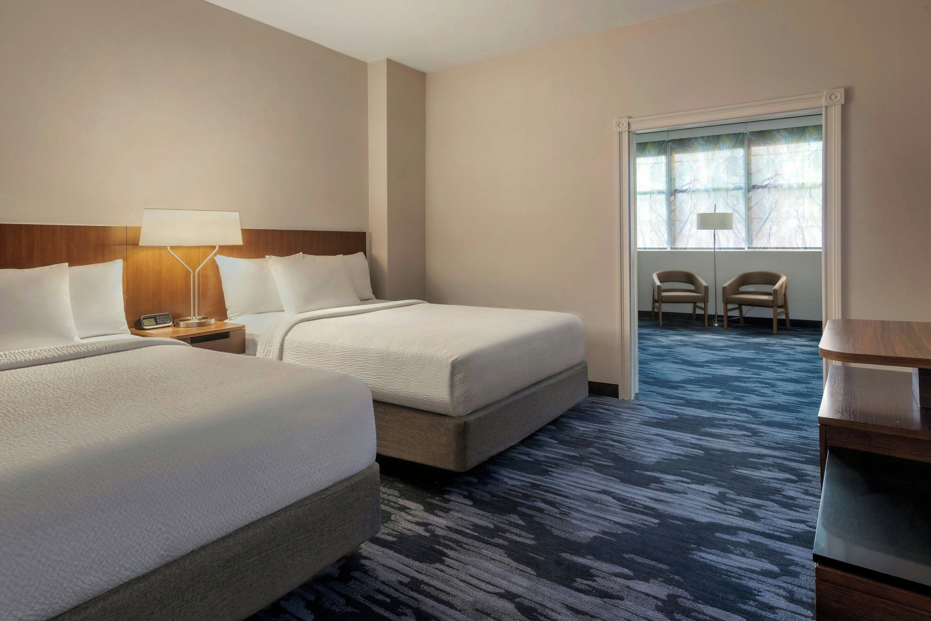 A hotel room with two beds, a desk, a chair, and a window with a view.