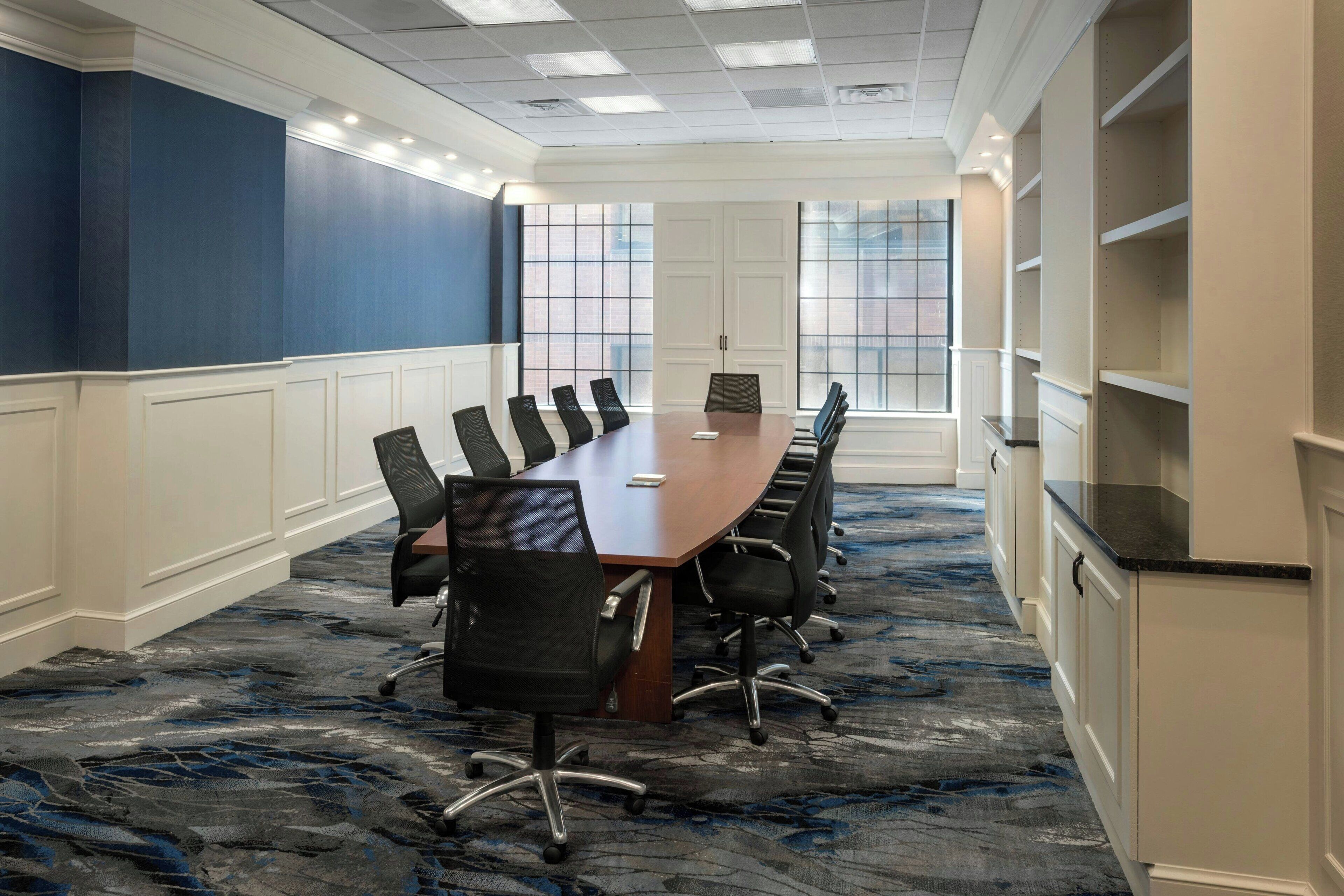 A conference room with a long table, black chairs, and a carpeted floor.