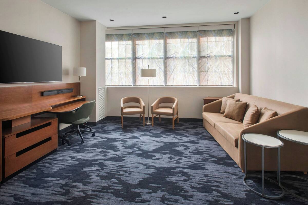 Ein modernes Hotelzimmer mit einem großen Flachbildfernseher, einem Holztisch, zwei Sesseln, einem Sofa und einem kleinen Tisch.