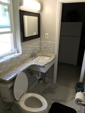 Bathroom features a toilet, sink, and mirror, with a window and subway tile walls.